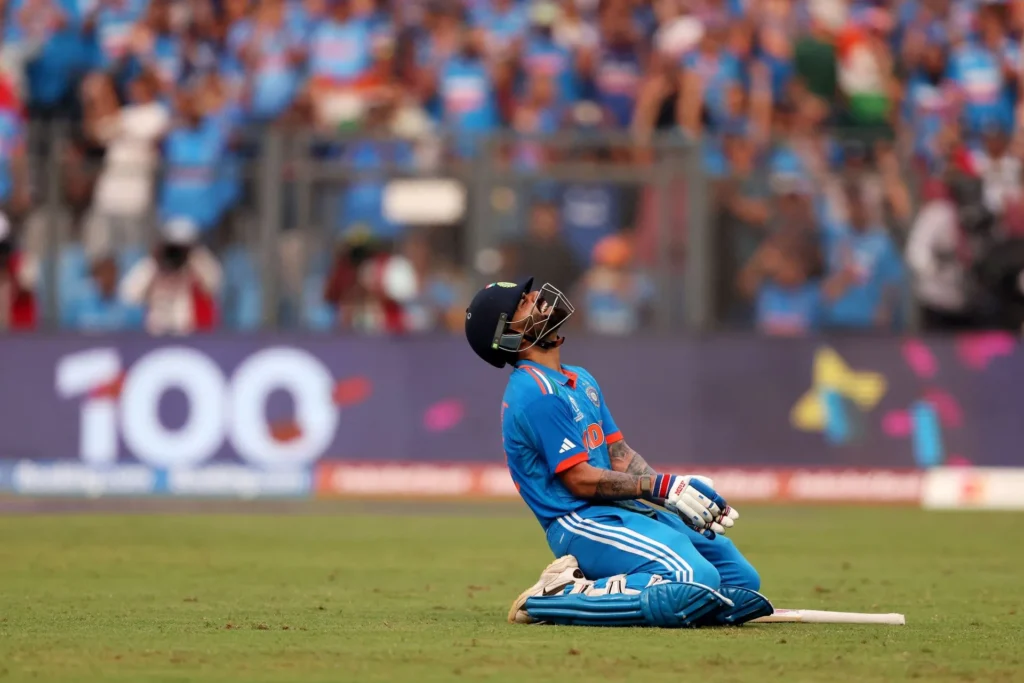 Virat Kohli smiling in a black suit with brand logos, symbolizing his net worth and endorsements in 2025